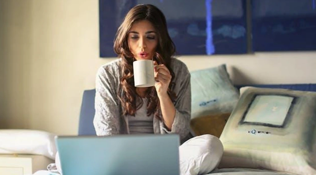 A woman holding a mug while using her laptop